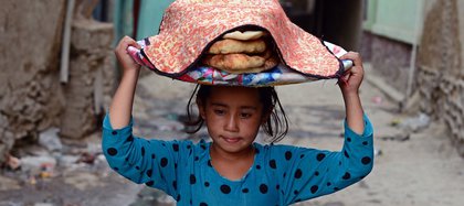 Una niña afgana lleva una canasta de pan en la cabeza en la parte antigua de Kabul el 2 de septiembre de 2014. La economía de Afganistán ha mejorado significativamente desde la caída del régimen talibán en 2001, en gran parte debido a la infusión de asistencia internacional. A pesar de la mejora significativa en la última década, el país sigue siendo extremadamente pobre y sigue dependiendo en gran medida de la ayuda exterior. (WAKIL KOHSAR / AFP / Getty Images)